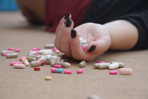 Drugs and pills are scattered on the floor and spill out of a lady's hand