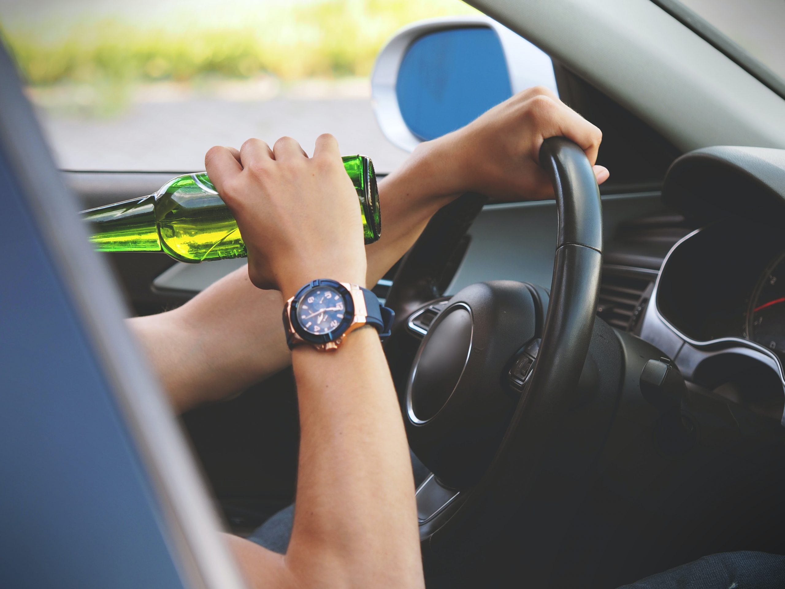 Picture of a person drinking beer while driving a car.